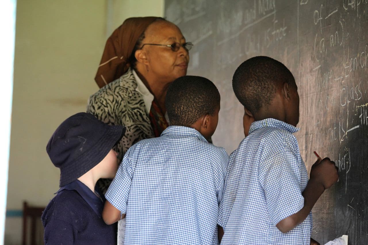 A teacher and three students standing next to a chalk board