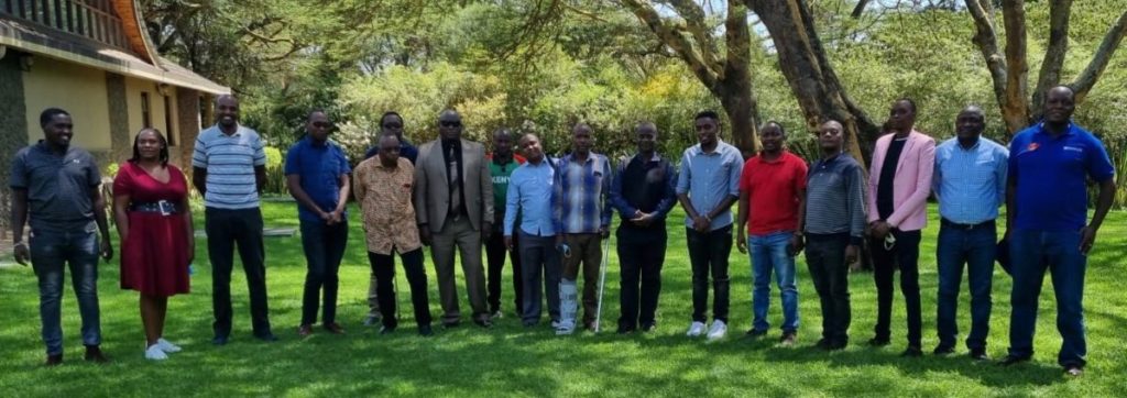 17 black men and 1 black woman stand together on grassy area outside meeting venue.