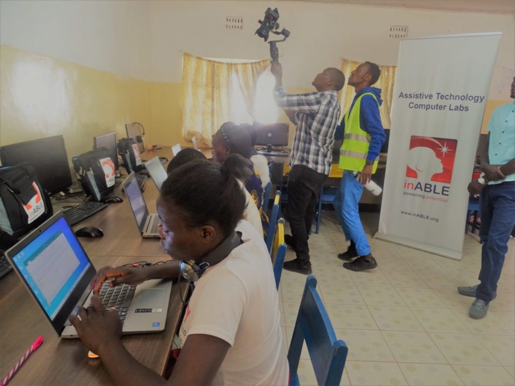 Girls face laptop computers as videographers crane camera over their heads to record their ICT training