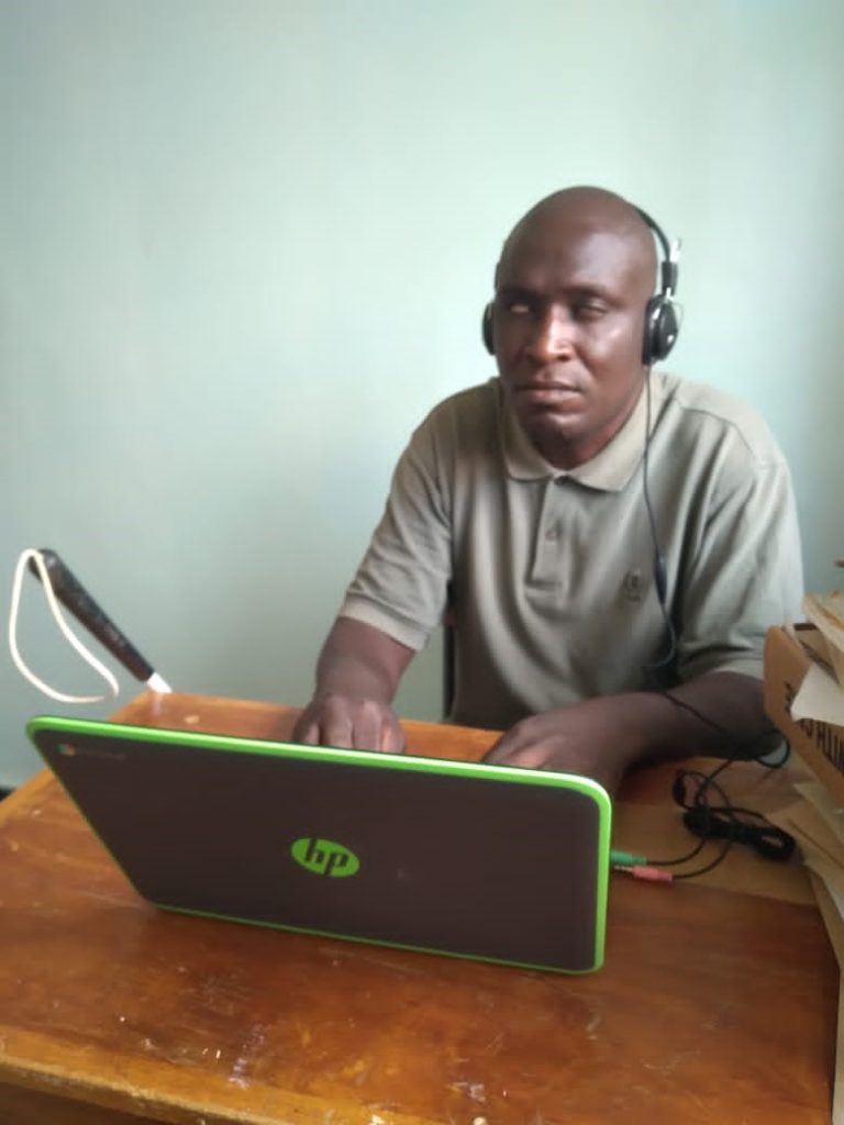 Lawi Obonyo faces forward wearing headphones and typing on HP laptop keyboard, while seated at a desk in the office.