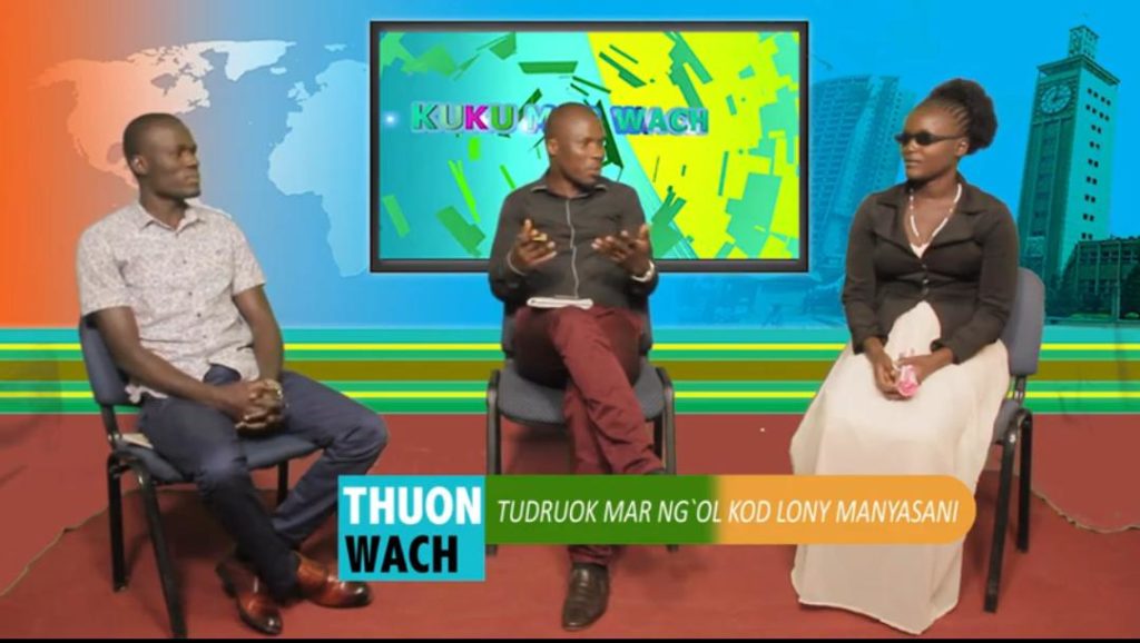 INABLE COMPUTER INSTRUCTOR SHADRACK OTIENO (LEFT), LOLWE TV HOST HARON OTIENO (CENTER), INABLE COMPUTER-LAB –FOR-THE-BLIND PROGRAM ALUMNI JOYCE ACHOLA (RIGHT) SIT IN FRONT OF COLORFUL SCREEN WITH CITY IMAGE BEHIND IT.