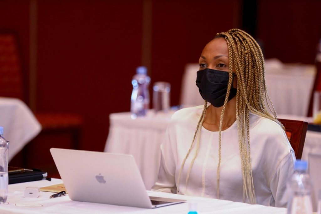 inABLE Executive Director Irene Mbari-Kirika sits at a conference table wearing black mask, white shirt and has a laptop computer open in front of her as she listens to a speaker