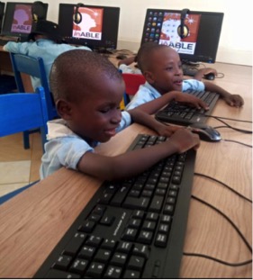 Two small black boys, wearing blue short sleeve shirts, reach up to touch computer keyboard