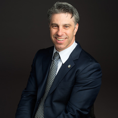 White Man with short gray hair wearing a white collar shirt and blue blazer smiles