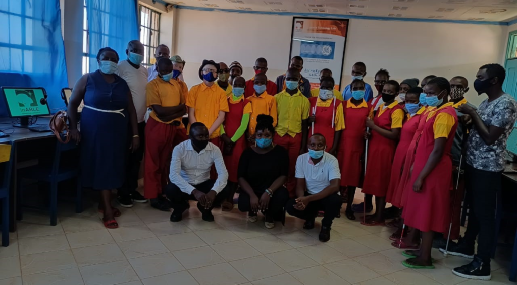 Class Eight candidates, wearing orange and red school uniforms, pose for a group photo with with their teachers and the inABLE Team inside the inABLE Computer Lab at St. Lucy School for the Blind 