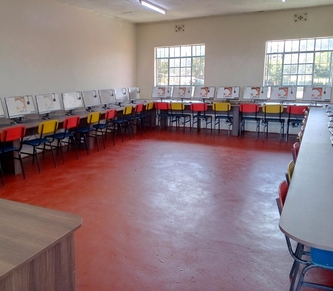A picture that shows inside St. Lucy’s High School Laboratory has long tables, chairs, and desktop monitors with headphones and keyboards.