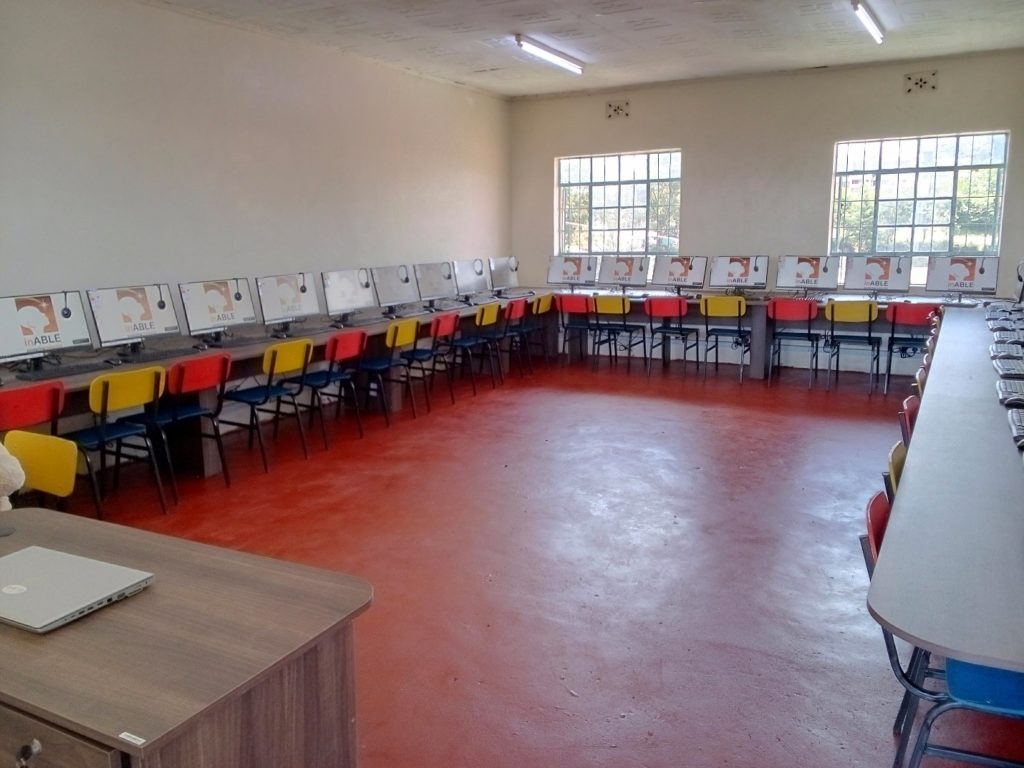 A picture that shows inside St. Lucy's High School Laboratory has long tables, chairs, and desktop monitors with headphones and keyboards.