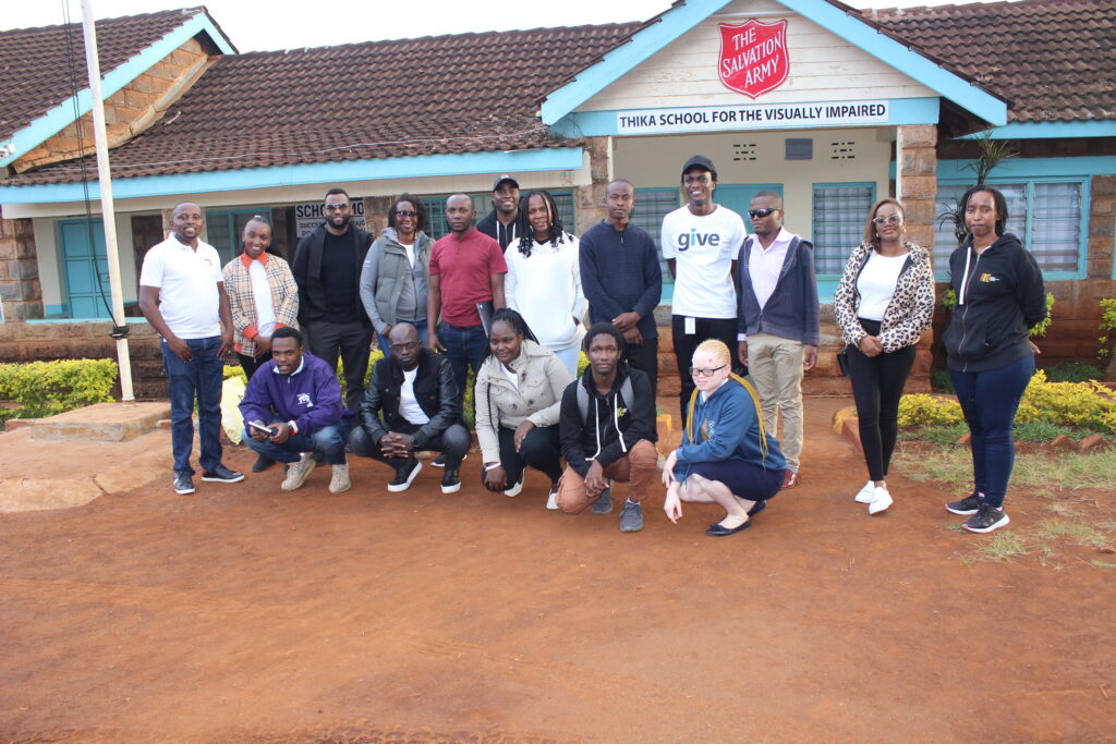 A picture of the inABLE and Microsoft Staff, smiling and posting for a picture. Behind them a sign is written Thika School For the Visually Impaired, The Salvation Army.