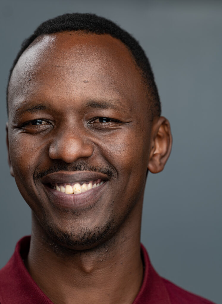 A passport picture of Jules smiling and posing. He's wearing a dark red shirt and his eyes are open.