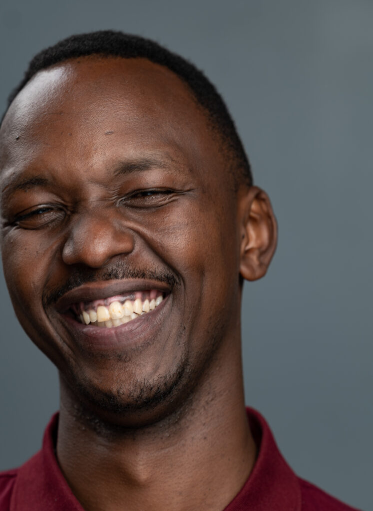 A passport picture of Jules smiling and posing. He's wearing a dark red shirt and his eyes are closed.