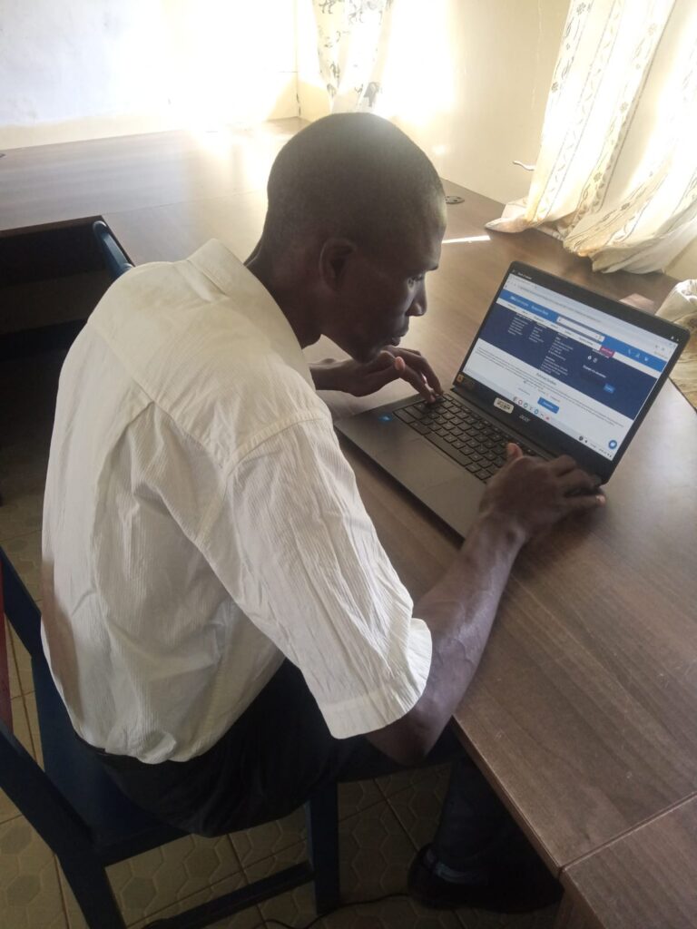 A picture of Mr. Joash Ododa seated on a chair and using a laptop.