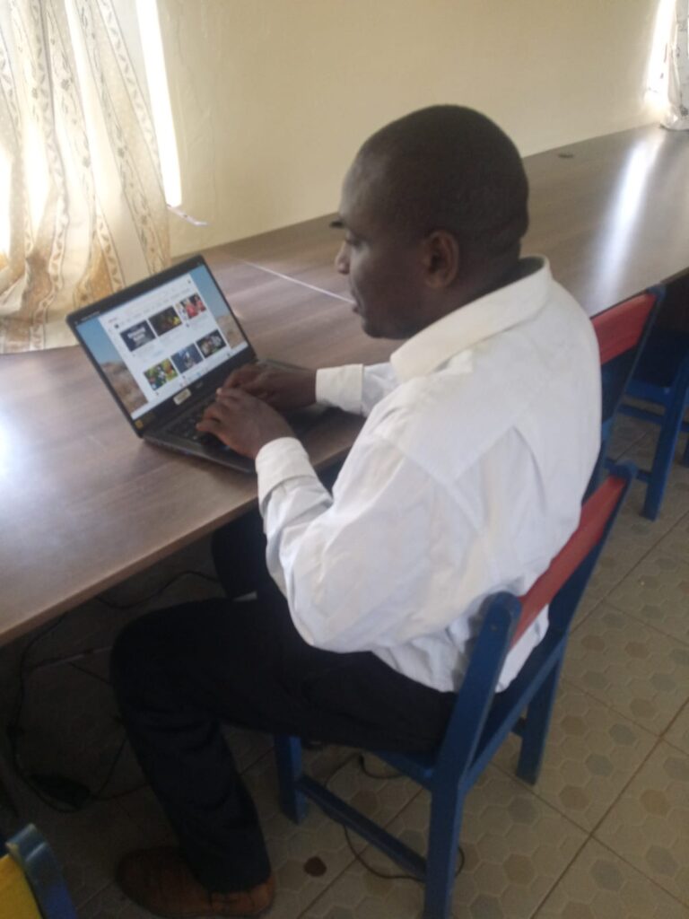 A picture of Mr. Lawi Obonyo seated on a chair and typing on a laptop.