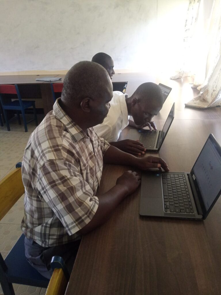 A picture of Mr. Joash Ododa, Mr. Fredrick Ochieng, and Mr. Lawi Obonyo seated next to each other. They're all using laptops.