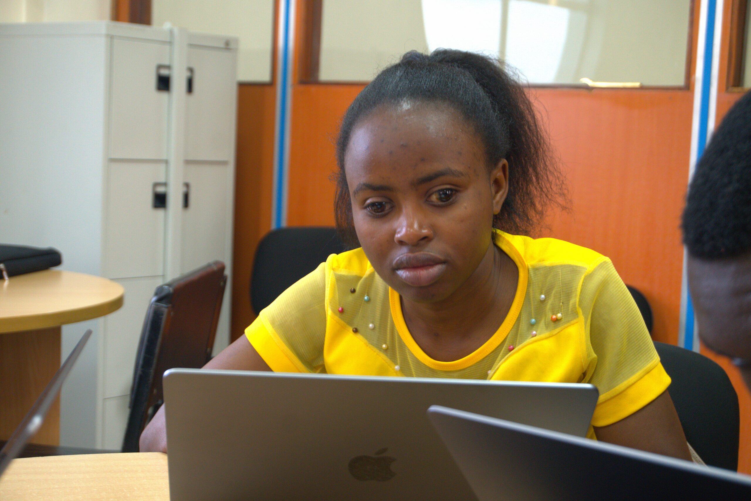 A Brenda Mwende seated on a chair using a Macbook laptop.