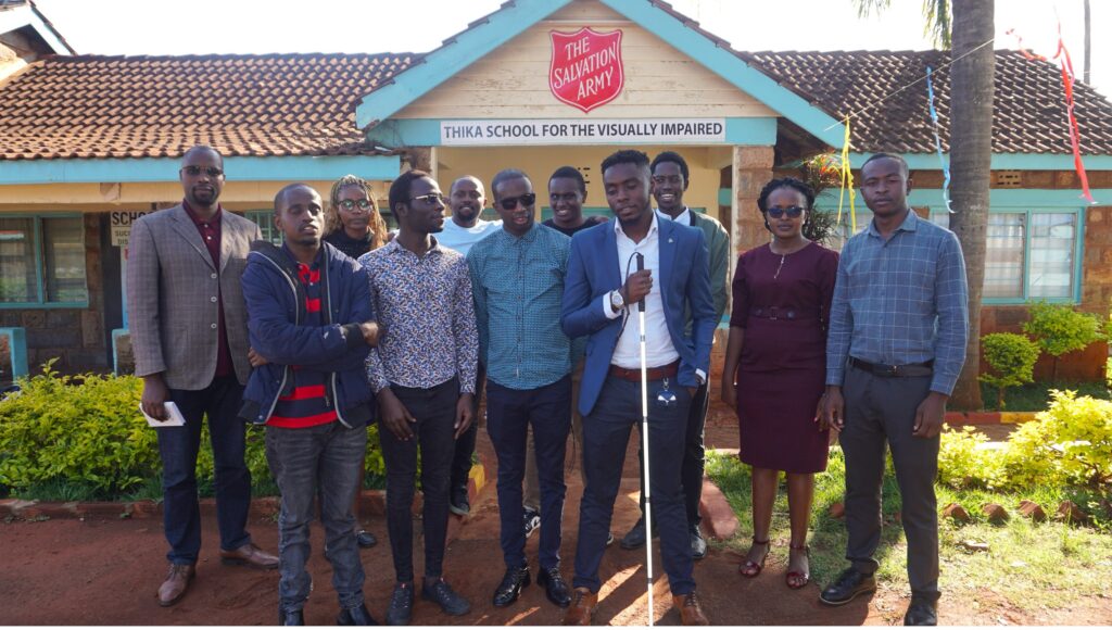 A group of adults, including inABLE staff and USIU students, pose for a photo in front of the administration block at Thika School for the Visually Impaired. The visit was a courtesy call to students participating in a coding bootcamp.