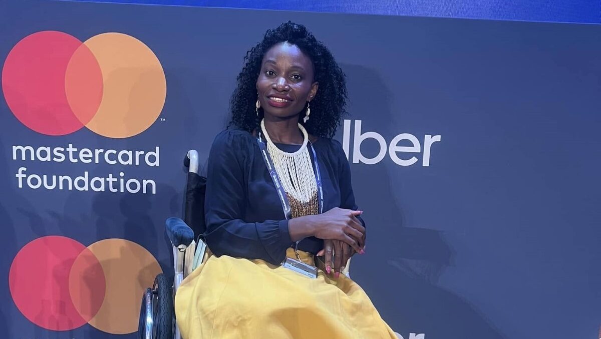 Victo posing for a picture in front of a banner with Mastercard Foundation and Uber logo during the Inclusive Africa Conference 2024