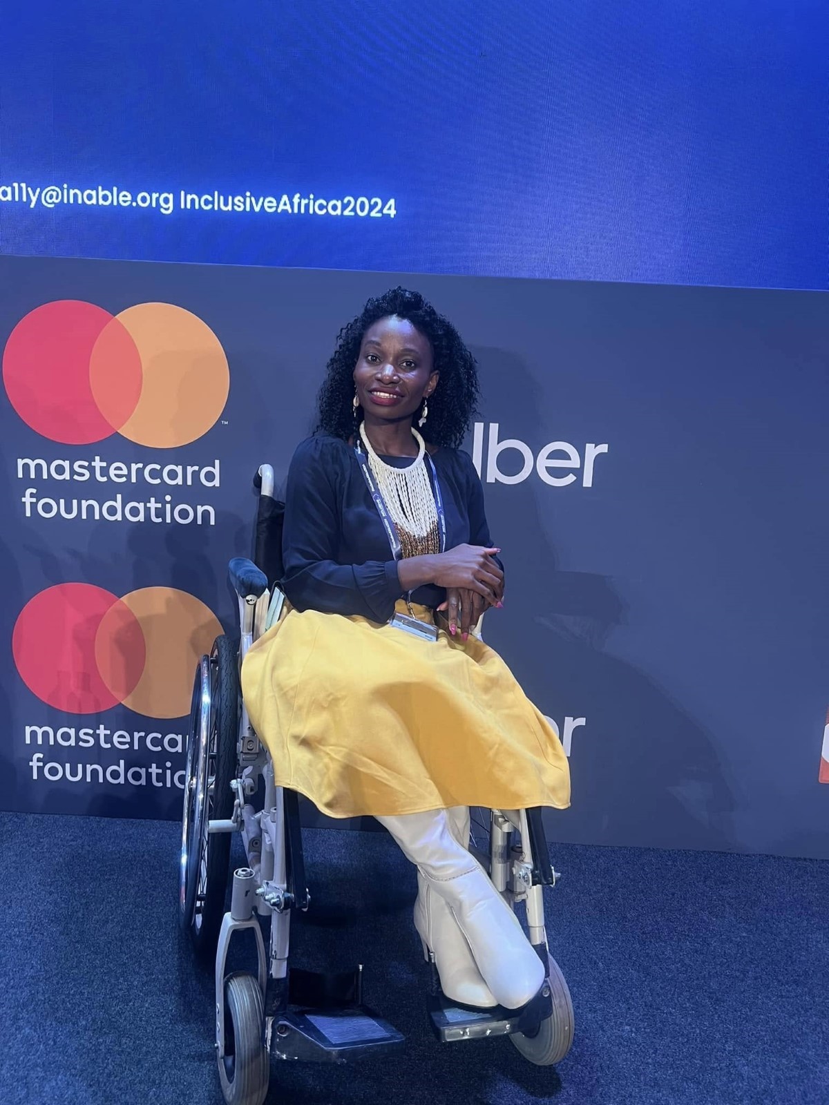 Victo posing for a picture in front of a banner with Mastercard Foundation and Uber logo during the Inclusive Africa Conference 2024