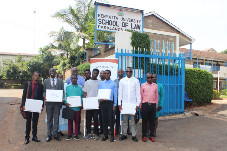 A group of beneficiaries of the MacBook program are standing outside a building labeled 