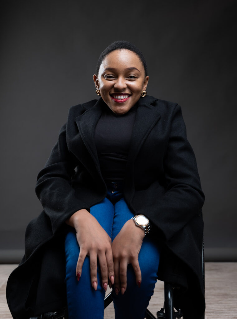 A picture of Mumsie, in a wheelchair, smiling at the camera, showcasing her joyful spirit and vibrant personality.